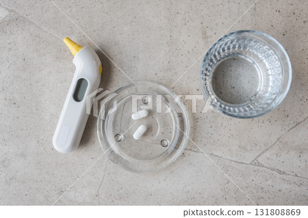 White digital thermometer for temperature, pill and glass with water on the stone table. Healthcare from pharmacy. Person sit at home because of illness. White digital thermometer for temperature, pill and glass with water on the stone table. Healthcare from pharmacy. Person sit at home because of illness. 131808869
