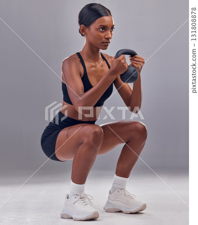 Woman, kettlebell squats and exercise in studio for fitness, sports workout and focus wellness mindset. Strong female, bodybuilder or weights training for muscle power, energy or health on background 131808878