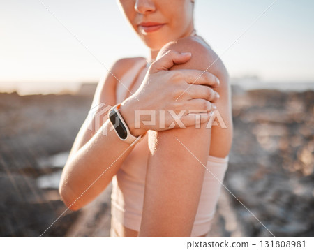 Beach, fitness and woman with hand on shoulder pain standing on rocks at ocean. Nature, sports and injury during workout for health and wellness, muscle trauma during stretching exercise in morning. 131808981