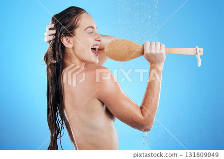 Shower singing, skincare and woman with happiness karaoke in a studio. Bathroom, music and happy wet female model with isolated blue background and cleaning brush for beauty routine, wellness and fun Shower singing, skincare and woman with happiness karaoke in a studio. Bathroom, music and happy wet female model with isolated blue background and cleaning brush for beauty routine, wellness and fun 131809049