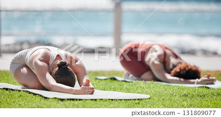 Woman, yoga friends and stretching on grass for wellness, strong legs and body in morning sunshine by sea. Women teamwork, fitness and workout by ocean with support, focus and mindfulness in summer 131809077