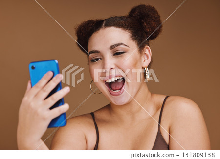 Phone, selfie and face of woman with smile on brown background for wellness, fashion and makeup. Wow, video call and happy girl influencer on smartphone for social media, internet and online post 131809138