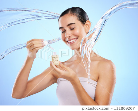 Happy woman, dropper and water splash for skincare serum, product or hygiene against blue studio background. Calm female smile holding pipette for beauty cosmetics, essential oil or facial treatment 131809207