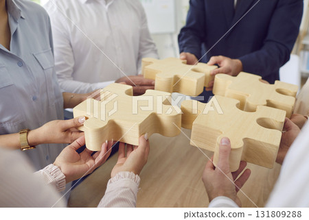 Team of business people connecting wooden jigsaw puzzle parts as symbol of teamwork 131809288