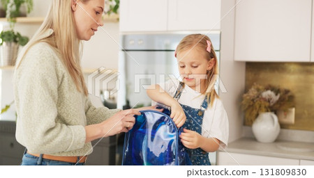 Backpack, kitchen and mother with girl for school, education and ready for class in morning. Happy family, parents and mom with child prepare lunch, snack and books in bag for childhood learning 131809830