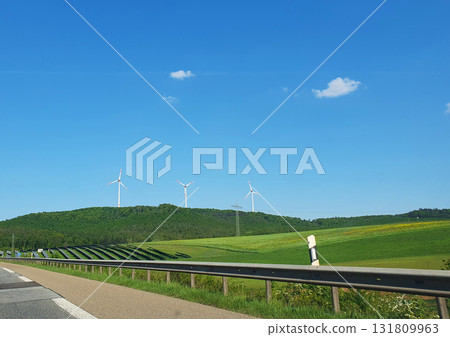 Three white windmills with green field and blue sky. Wind turbine and solar panels (solar cell) in solar farm for alternative green energy in Europe. Three white windmills with green field and blue sky. Wind turbine and solar panels (solar cell) in solar farm for alternative green energy in Europe. 131809963