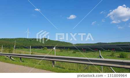 Three white windmills with green field and blue sky. Wind turbine and solar panels (solar cell) in solar farm for alternative green energy in Europe.  131809964