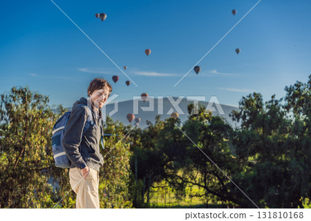 Male tourist standing with colorful hot air balloons floating in the sky behind him, enjoying adventure and sightseeing over Mexico. Travel, tourism, and exploration concept Male tourist standing with colorful hot air balloons floating in the sky behind him, enjoying adventure and sightseeing over Mexico. Travel, tourism, and exploration concept 131810168