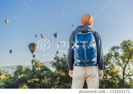 Male tourist standing with colorful hot air balloons floating in the sky behind him, enjoying adventure and sightseeing over Mexico. Travel, tourism, and exploration concept Male tourist standing with colorful hot air balloons floating in the sky behind him, enjoying adventure and sightseeing over Mexico. Travel, tourism, and exploration concept 131810172