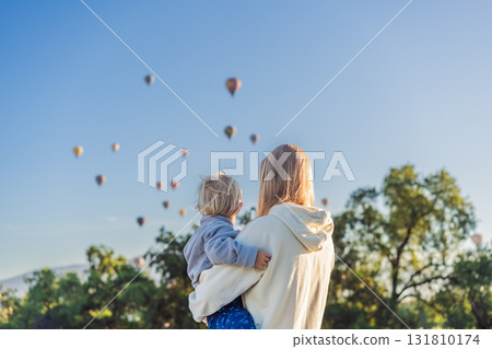 Mother with her young son as tourists, standing with colorful hot air balloons floating behind them over Teotihuacan, Mexico. Family travel, adventure, and cultural exploration concept 131810174