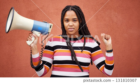 Protest, megaphone and portrait of a woman by a wall in the city for freedom, equality and human rights. Fist, speaker and African female fighting at a rally for justice, democracy and racism in town Protest, megaphone and portrait of a woman by a wall in the city for freedom, equality and human rights. Fist, speaker and African female fighting at a rally for justice, democracy and racism in town 131810307