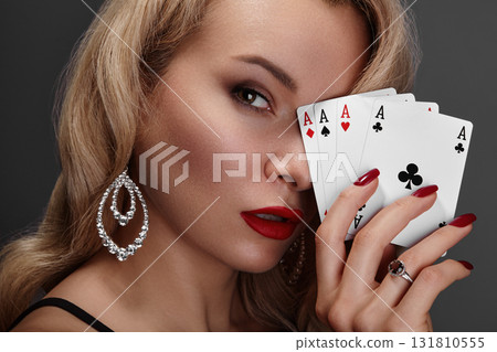 Blonde lady woman in black shiny dress and expensive diamond jewelry is winner money from Omaha Holdem. She is smiling, showing Aces cards to the camera. Ideal style for Poker, Casino, Gambling 131810555