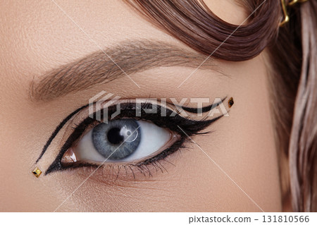 Close-up macro of a blue eye with dramatic black winged eyeliner and precise graphic lines, sharp studio lighting emphasizing lash with eye liner, pigment and editorial beauty makeup 131810566