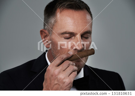 Wealth, vintage and face of man with cigars for smoking habit on gray background for luxury, power and success. Retirement, business gangster and senior male smell tobacco smoke for rich lifestyle Wealth, vintage and face of man with cigars for smoking habit on gray background for luxury, power and success. Retirement, business gangster and senior male smell tobacco smoke for rich lifestyle 131810631