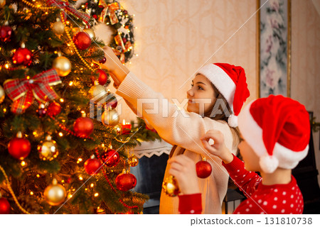 Teenage girl decorating Christmas tree, her younger brother helps her, holding baubles. Cheerful children decorating Christmas tree at home 131810738