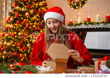 Young girl opens Christmas present. Surprised blonde girl in decorated living room opens box gift from friend for Christmas Young girl opens Christmas present. Surprised blonde girl in decorated living room opens box gift from friend for Christmas 131810747