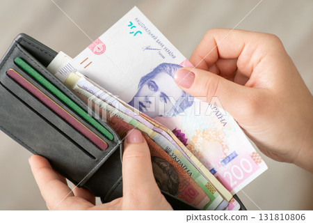 Grey wallet with ukrainian hryvnias, female hand takes one banknote out there. Concept of money, cash, shopping Grey wallet with ukrainian hryvnias, female hand takes one banknote out there. Concept of money, cash, shopping 131810806