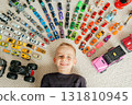 Happy child framed by lines of miniature vehicles on carpet, bright toys and cheerful expression create playful composition 131810945