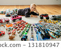 Top-down view of a boy lying on the floor surrounded by a vast, colorful collection of toy cars neatly arranged in rows childhood hobby and play 131810947
