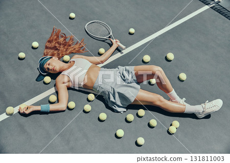 Fashion, tennis and woman lying on the court with a racket and balls after a game or practice. Fitness, sports and portrait of a female athlete relaxing at the outdoor stadium after match or training 131811003