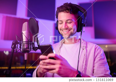 Man, phone and smile in music studio chatting, social media or podcast post at the workplace. Happy male auto tuner smiling on smartphone for networking, sound track or listening in sound proof room Man, phone and smile in music studio chatting, social media or podcast post at the workplace. Happy male auto tuner smiling on smartphone for networking, sound track or listening in sound proof room 131811069