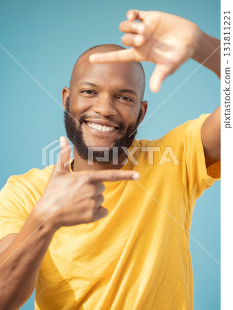Hands, frame and portrait of black man on blue background for profile picture. Face, happy guy and finger framing for perspective, selfie and vision of happiness, smile and photography sign in studio 131811221