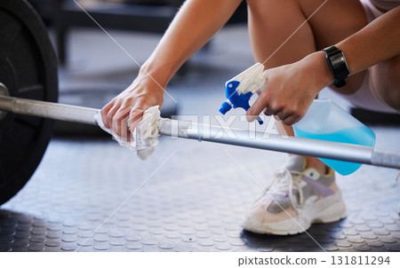 Hands, weight and covid with a gym worker spraying exercise equipment with sanitizer or disinfectant. Cleaning, bacteria and liquid with an employee at work in a sports clinic for fitness hygiene Hands, weight and covid with a gym worker spraying exercise equipment with sanitizer or disinfectant. Cleaning, bacteria and liquid with an employee at work in a sports clinic for fitness hygiene 131811294