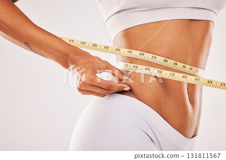 Weight, fat and woman with tape for stomach isolated on a grey studio background. Insecurity, health and girl measuring her body for slim shape, cellulite and belly while standing on a backdrop Weight, fat and woman with tape for stomach isolated on a grey studio background. Insecurity, health and girl measuring her body for slim shape, cellulite and belly while standing on a backdrop 131811567