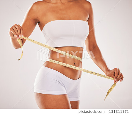 Lose weight, body and woman with tape for stomach isolated on a grey studio background. Diet, health and girl measuring her waist for slim shape, motivation and belly while standing on a backdrop 131811571