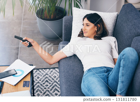 Television, relax and a woman on a sofa in the living room of her home streaming a subscription service. Watching tv, channel surfing and comedy with an attractive young female lying in her lounge Television, relax and a woman on a sofa in the living room of her home streaming a subscription service. Watching tv, channel surfing and comedy with an attractive young female lying in her lounge 131811780