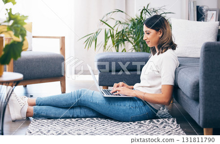 Woman, laptop and typing sitting on floor in the living room by sofa in remote work or studying at home. Female freelancer working on computer checking email, research or browsing in lounge by couch Woman, laptop and typing sitting on floor in the living room by sofa in remote work or studying at home. Female freelancer working on computer checking email, research or browsing in lounge by couch 131811790