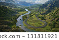 Serpentine road winds through lush green mountain valley beside flowing river and distant snow capped peaks 131811921