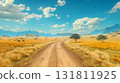 A winding dirt road through a golden savanna landscape with distant mountains and grazing cattle 131811925