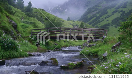 A wooden bridge spans a flowing stream amidst green hills and misty mountains A wooden bridge spans a flowing stream amidst green hills and misty mountains 131811935