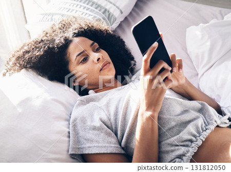 Black woman, sad and typing with phone on bed in home bedroom for social media or internet browsing in the morning. Technology, bored and lonely female with mobile for web scrolling or networking. 131812050