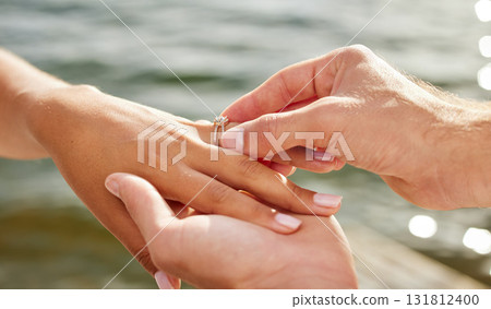Hands, proposal and engagement ring at lake outdoors for couple, marriage and wedding. Commitment, love and jewelry of woman and man proposing and putting band on finger for trust, care and romance. 131812400