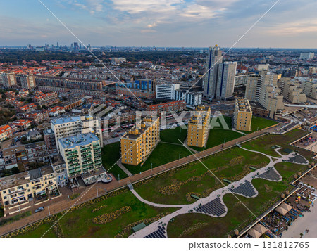 Hague, South Holland, Netherlands - 09.06.2025: Aerial view of coastal city with angular golden brown buildings on green lawn, beach promenade, and dense urban sprawl blending modern Hague, South Holland, Netherlands - 09.06.2025: Aerial view of coastal city with angular golden brown buildings on green lawn, beach promenade, and dense urban sprawl blending modern 131812765