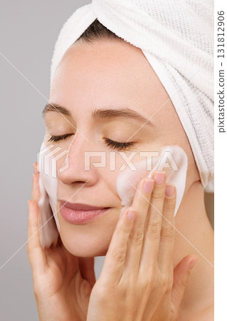 Adverstiring face cleansing foam. Closed eyes. Woman using moisturizing foam for face washing and smiling, morning skincare routine. Studio isolated Grey Background. Beauty routine. Skincare treatment Adverstiring face cleansing foam. Closed eyes. Woman using moisturizing foam for face washing and smiling, morning skincare routine. Studio isolated Grey Background. Beauty routine. Skincare treatment 131812906