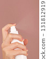 Vertical skincare ad. A woman's hand sprays facial mist, thermal water, or facial toner. The spraying process tones, refreshes, moisturizes, soothes facial skin. Pink backdrop. Copy space  131812919