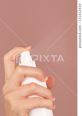Vertical skincare ad. A woman's hand sprays facial mist, thermal water, or facial toner. The spraying process tones, refreshes, moisturizes, soothes facial skin. Pink backdrop. Copy space Vertical skincare ad. A woman's hand sprays facial mist, thermal water, or facial toner. The spraying process tones, refreshes, moisturizes, soothes facial skin. Pink backdrop. Copy space 131812919