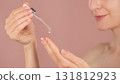 Woman applying cosmetic serum with dropper onto hand. Skincare product testing ads, beauty routine concept. Close-up of female hands with pipette, transparent liquid against pink background 131812923