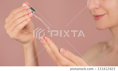 Woman applying cosmetic serum with dropper onto hand. Skincare product testing ads, beauty routine concept. Close-up of female hands with pipette, transparent liquid against pink background Woman applying cosmetic serum with dropper onto hand. Skincare product testing ads, beauty routine concept. Close-up of female hands with pipette, transparent liquid against pink background 131812923