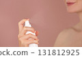 Skincare ads. Young woman sprays a facial spray mist or thermal water, face toner, facial tonic. Spraying process. Toning, refreshing, moisturizing, soothing skin. Pink background. Copy space  131812925