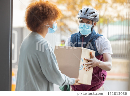 Black man, mask and delivery with box for woman at house for logistics, cargo and safety from covid 19. Young african courier, package and shipping service with stock, helmet and e commerce in city 131813086