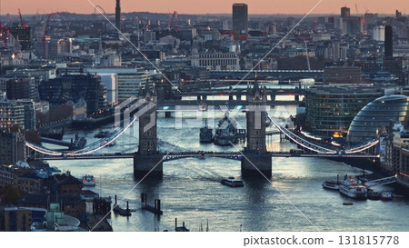Aerial view of Tower Bridge and HMS Belfast warship on River Thames at sunset, with London skyline cityscape in background, offering a captivating urban landscape. Travel to UK. Drone flight 131815778