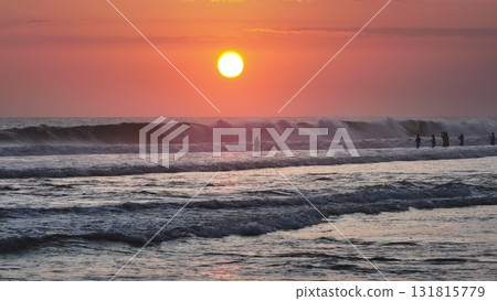 Local fishermen fishing in stormy ocean during colorful sunset in Bali, creating silhouettes against the vibrant pink sky, with huge waves crashing in the foreground. Beautiful nature background Local fishermen fishing in stormy ocean during colorful sunset in Bali, creating silhouettes against the vibrant pink sky, with huge waves crashing in the foreground. Beautiful nature background 131815779