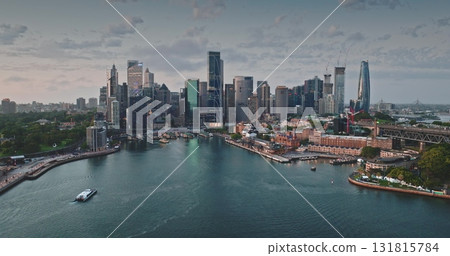 Australia, Sydney: Breathtaking aerial view of Sydney modern skyline city center reflecting in calm harbor waters. Iconic skyscrapers cityscape illuminated by soft sunset light. Drone panorama 131815784