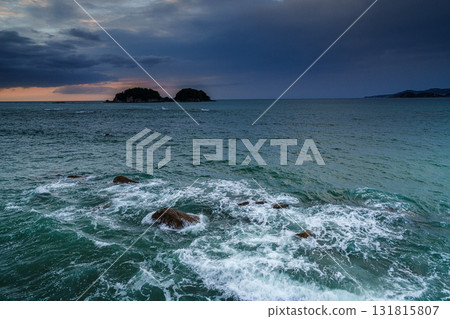 Sunset peeking through the clouds and white waves crashing on the rocks ⑪ 131815807