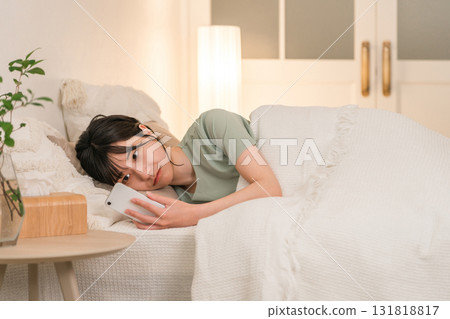 晚上，年輕的亞洲女性躺在床上看著她的智慧型手機 131818817