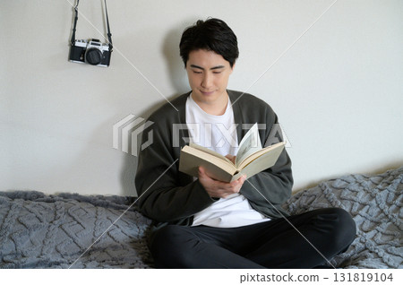Man sitting on bed reading a book Man sitting on bed reading a book 131819104